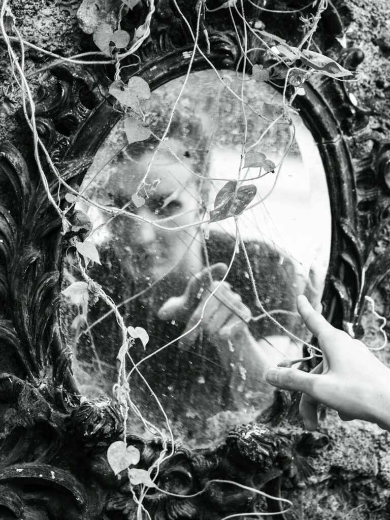 A moody black and white image capturing a reflection in a vintage mirror overgrown with ivy.