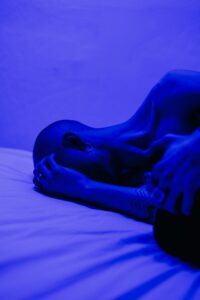 A tattooed man lying in blue light, symbolizing isolation and stress.